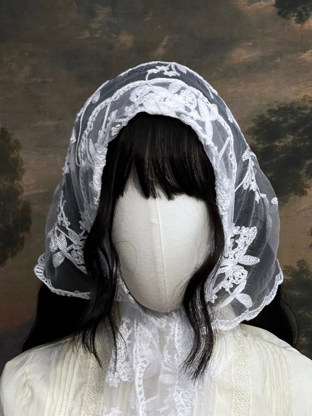 Mannequin wearing a vintage style white lace headscarf babushka triangle headdress made from floral embroidery lace against an art history background