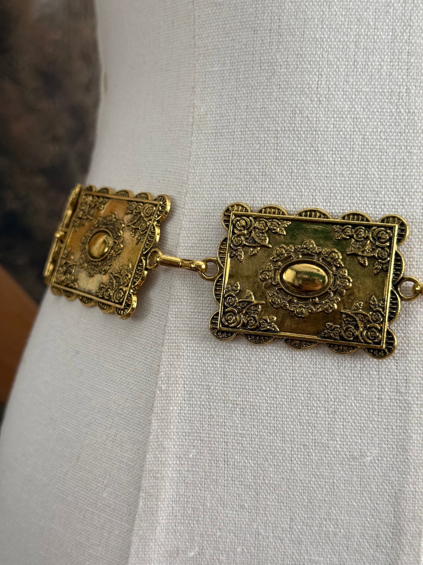 Historically inspired victorian era square concho style belt with rectangular gold toned metalwork, a scalloped edge, and floral motifs. Close up detail.