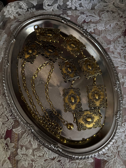Historically inspired victorian era square concho style belt with rectangular gold toned metalwork, a scalloped edge, and floral motifs. Sitting on a vintage silver tray