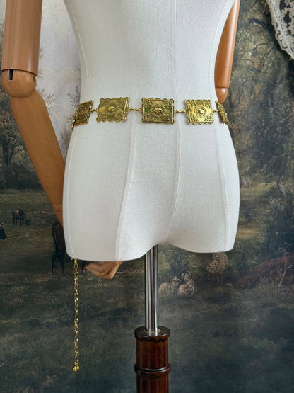 Historically inspired victorian era square concho style belt with rectangular gold toned metalwork, a scalloped edge, and floral motifs.