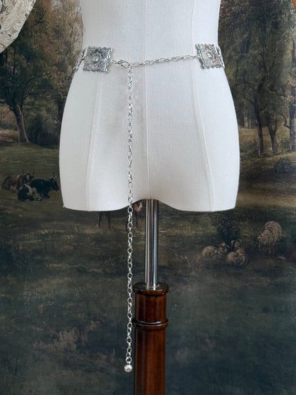 A silver concho style floral victorian metalwork rectangle chain belt pictured on a mannequin.