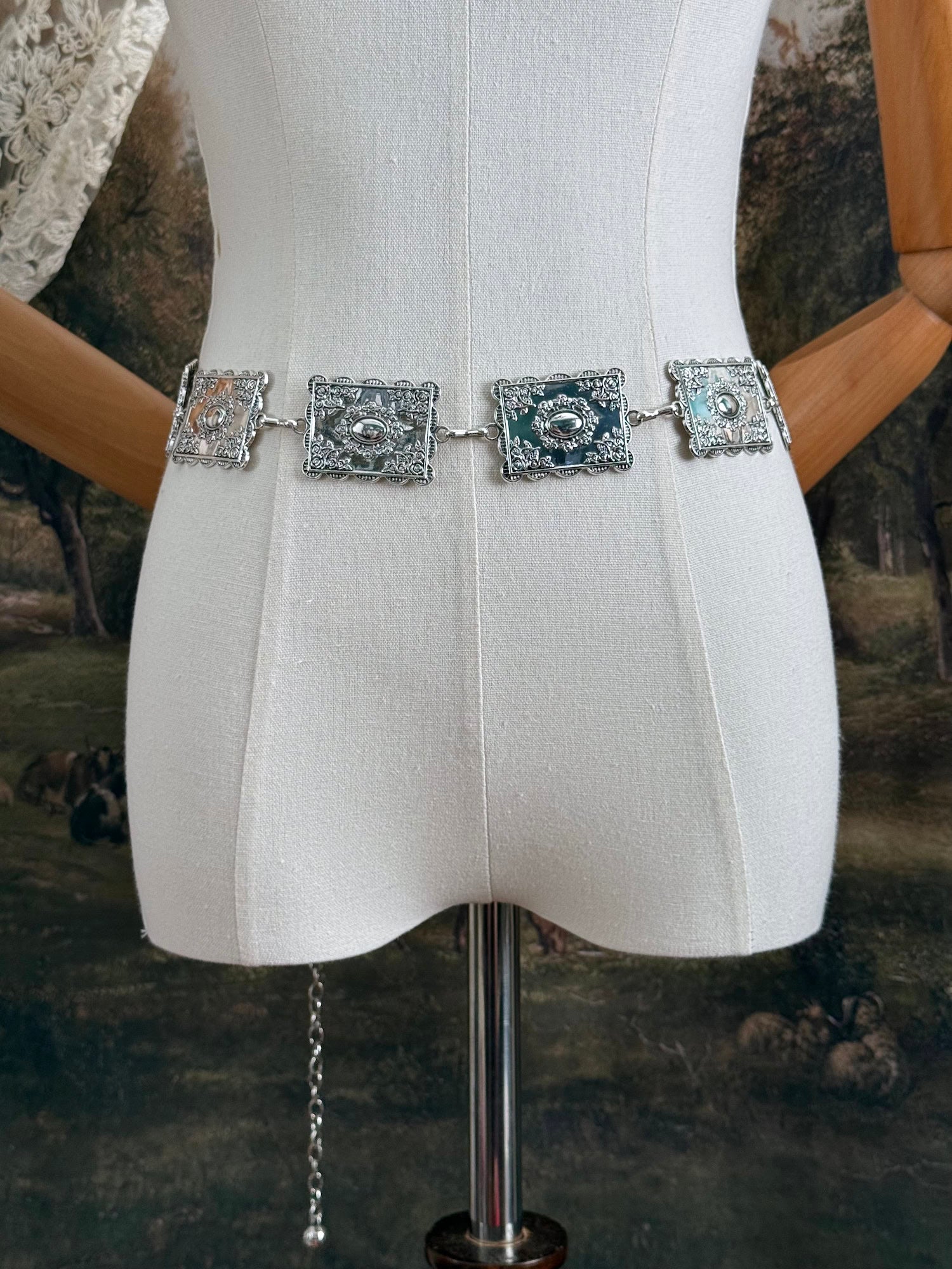A silver concho style floral victorian metalwork rectangle chain belt pictured on a mannequin.