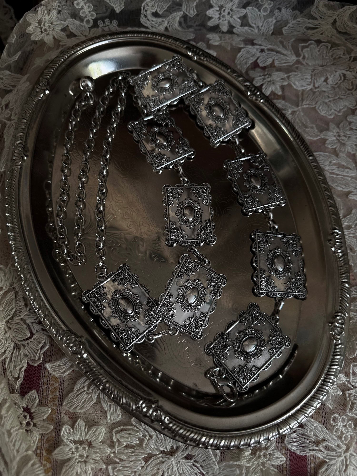 A silver concho style floral victorian metalwork rectangle chain belt pictured on a vintage silver tray