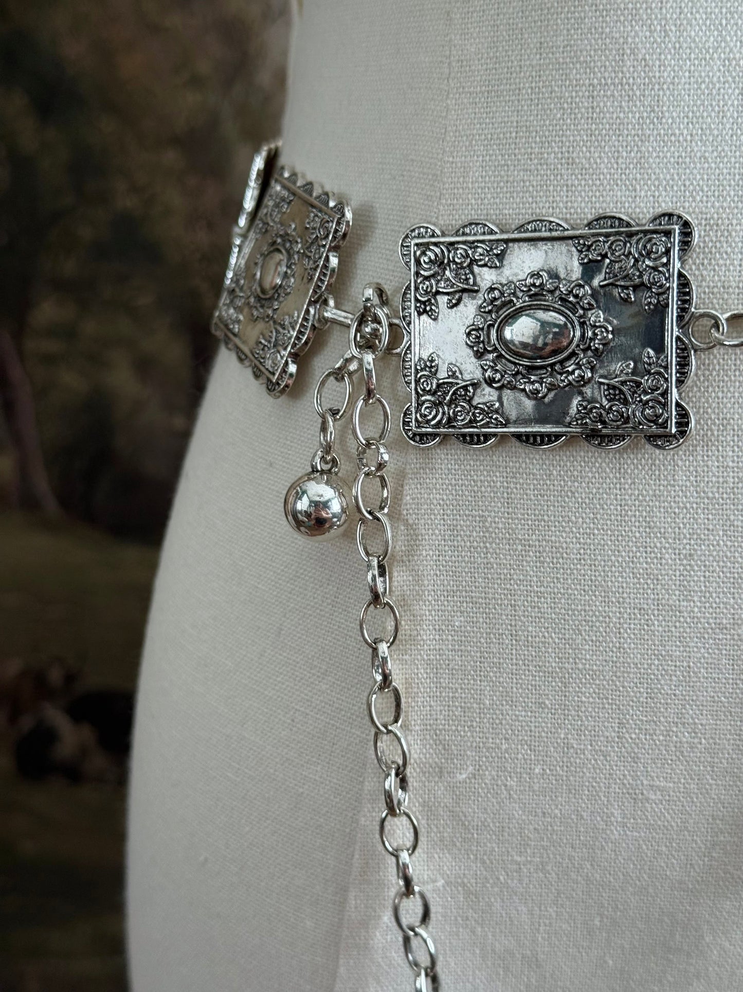 Up close detail of a silver concho style floral victorian metalwork rectangle chain belt pictured on a mannequin.