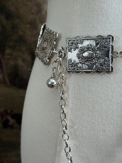 Up close detail of a silver concho style floral victorian metalwork rectangle chain belt pictured on a mannequin.