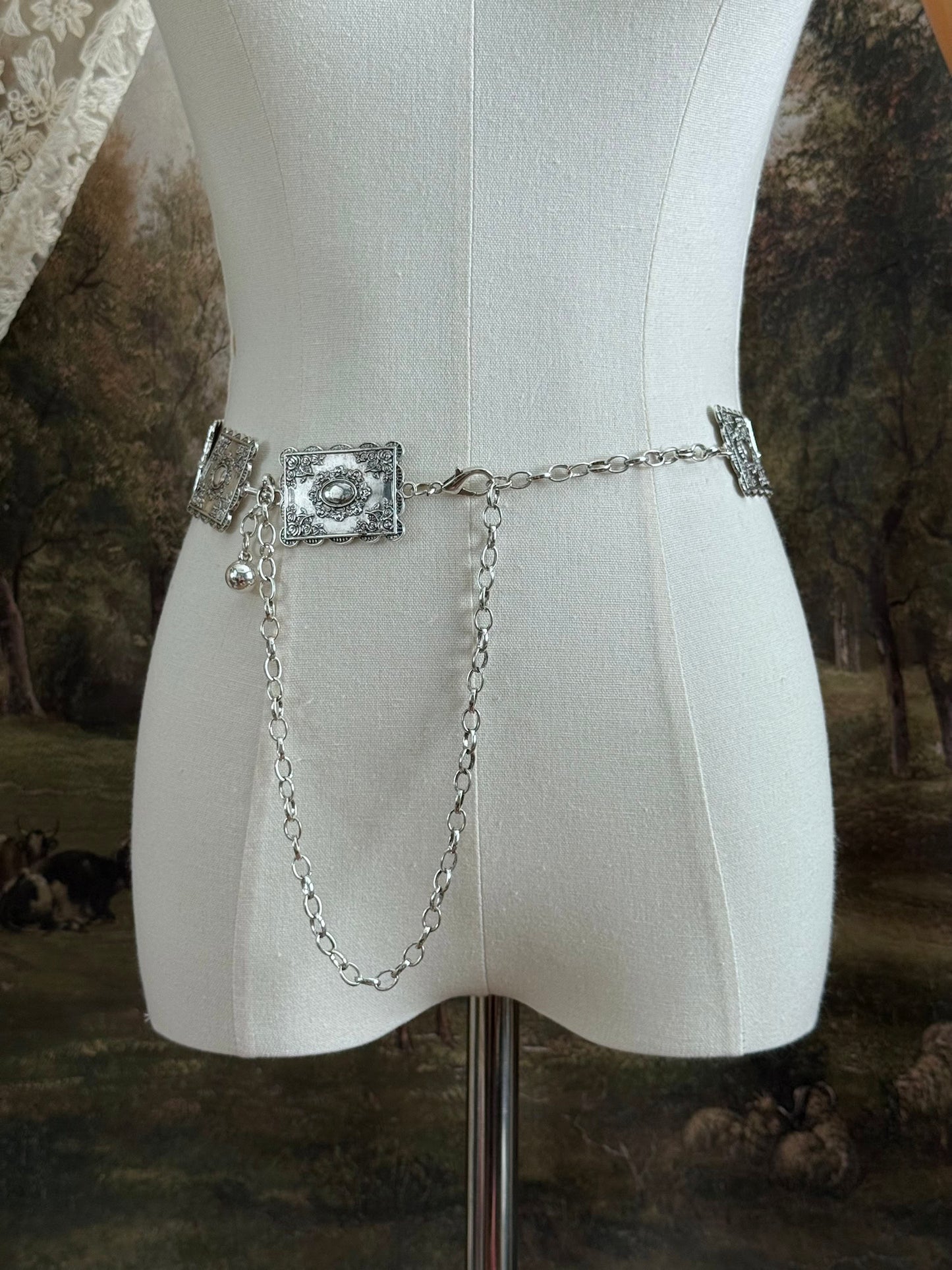 A silver concho style floral victorian metalwork rectangle chain belt pictured on a mannequin.