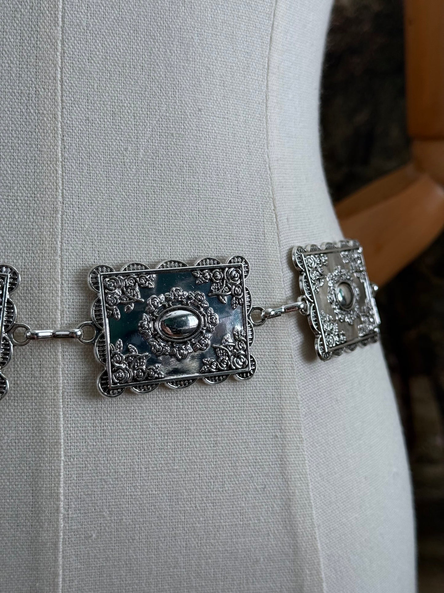 Up close detail of a silver concho style floral victorian metalwork rectangle chain belt pictured on a mannequin.