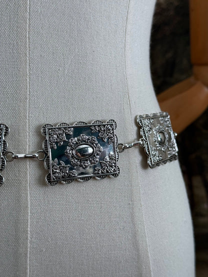 Up close detail of a silver concho style floral victorian metalwork rectangle chain belt pictured on a mannequin.