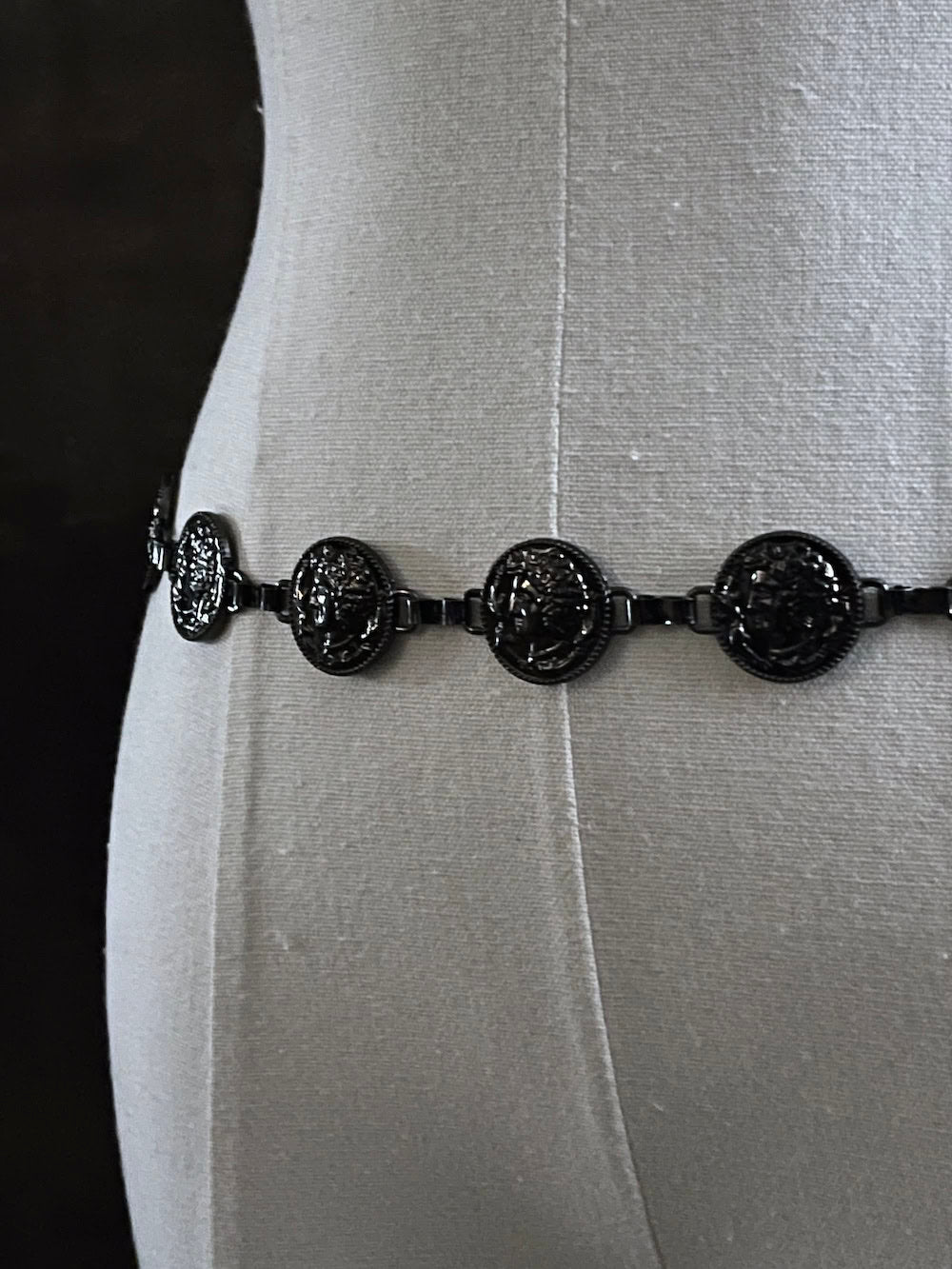 A historically inspired renaissance and medieval metal cameo coin belt in dark charcoal metal on a mannequin.