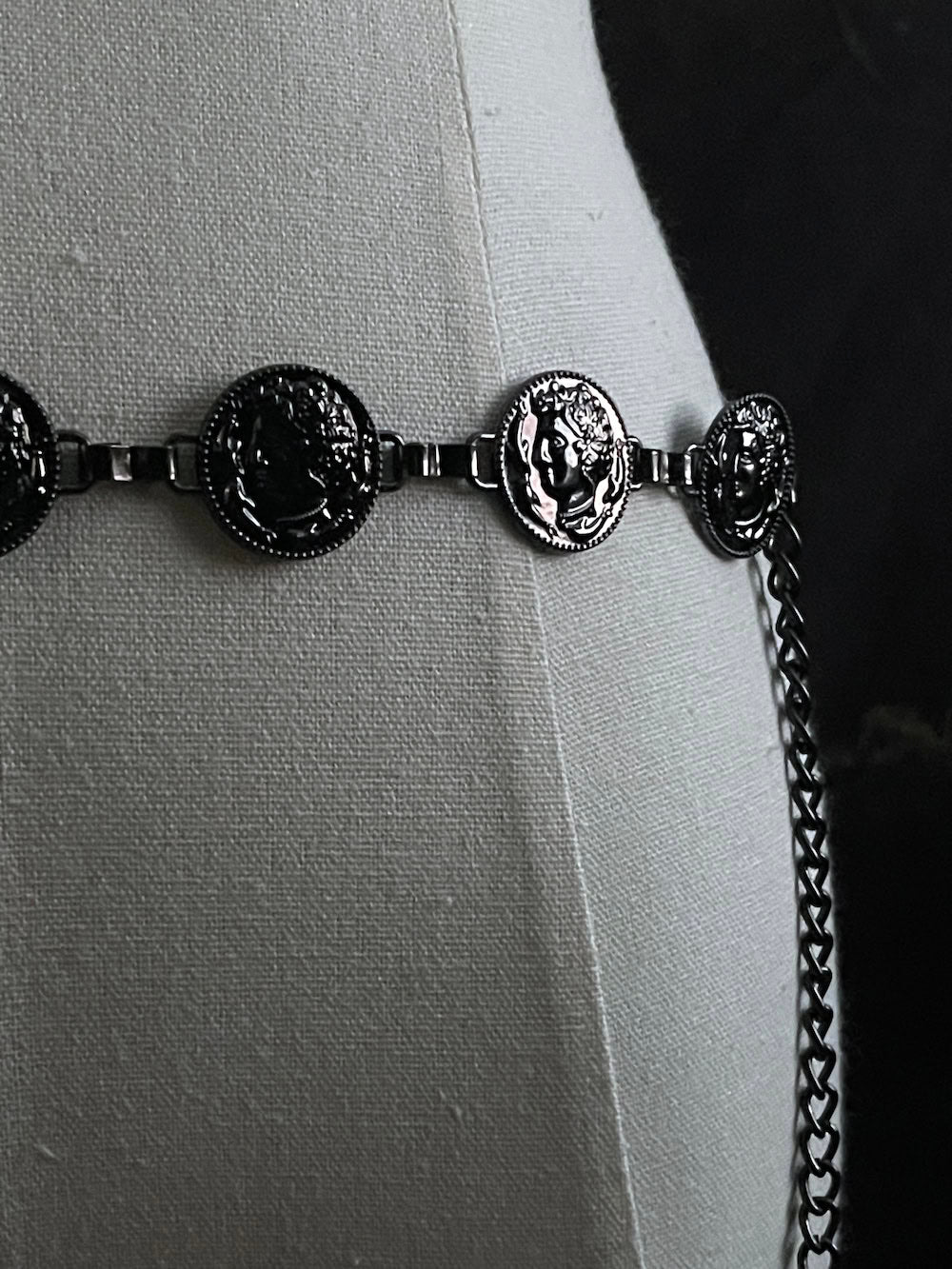 A historically inspired renaissance and medieval metal cameo coin belt in dark charcoal metal on a mannequin.
