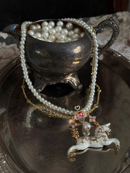 Handmade historical jewelry inspired pearl and chain necklace with a bejeweled medieval unicorn pendant, displayed on a silver tray.