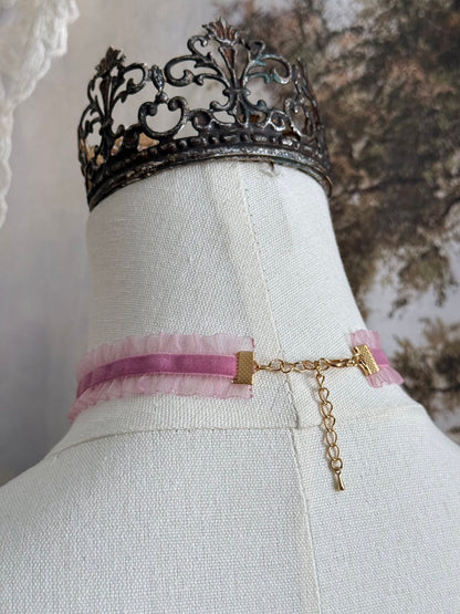 The clasp of a victorian fashion inspired mauve pink velveteen and chiffon ruffle lace choker necklace with a real rose bud charm and three faux pearl beads pictured on a mannequin