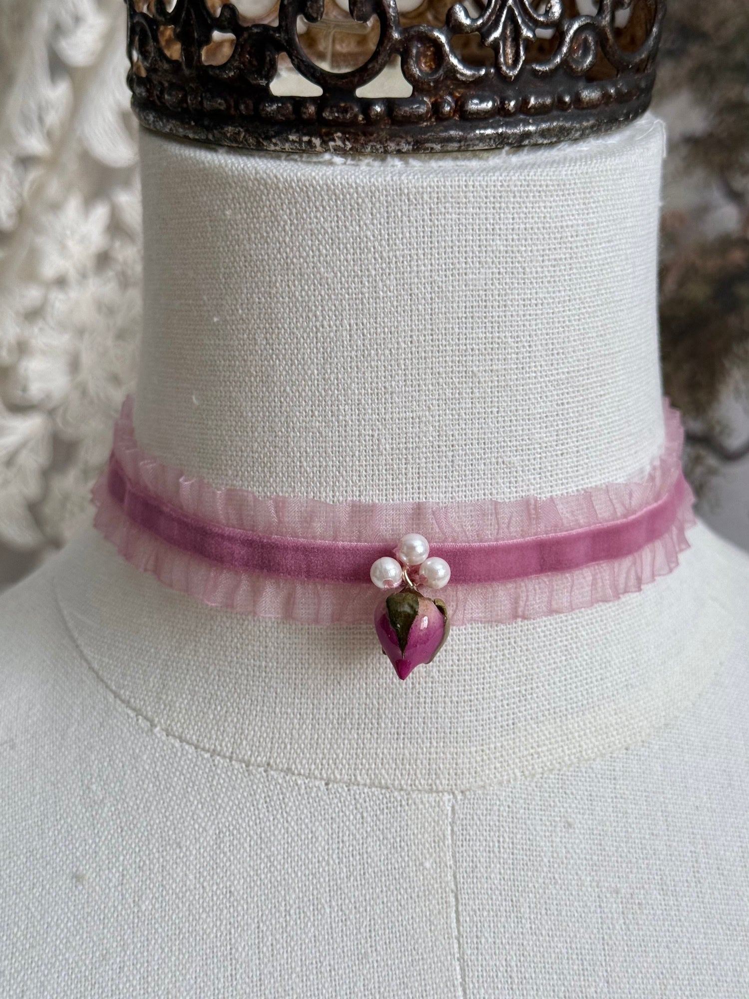 A victorian fashion inspired mauve pink velveteen and chiffon ruffle lace choker necklace with a real rose bud charm and three faux pearl beads pictured on a mannequin