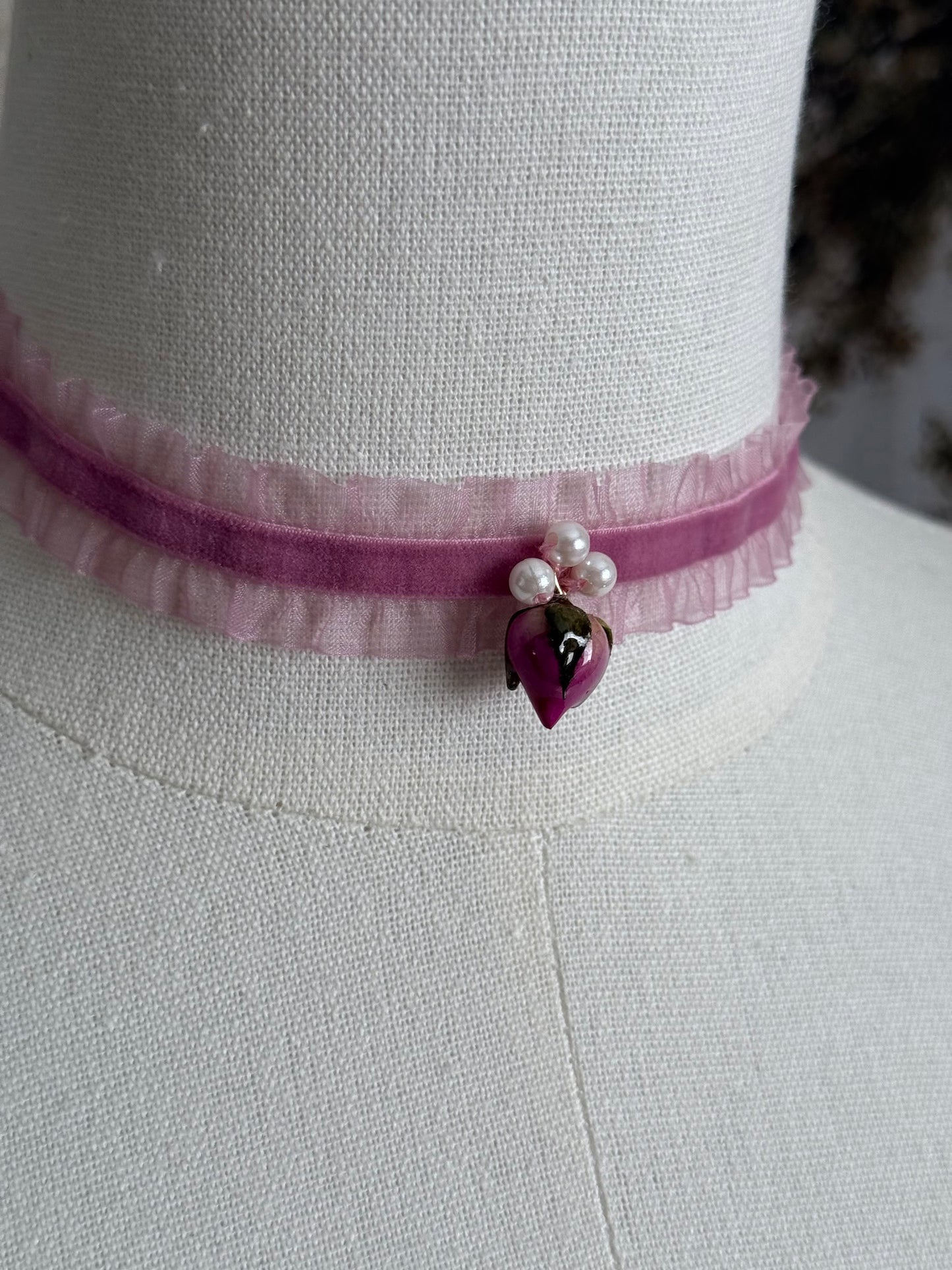 A victorian fashion inspired mauve pink velveteen and chiffon ruffle lace choker necklace with a real rose bud charm and three faux pearl beads pictured on a mannequin