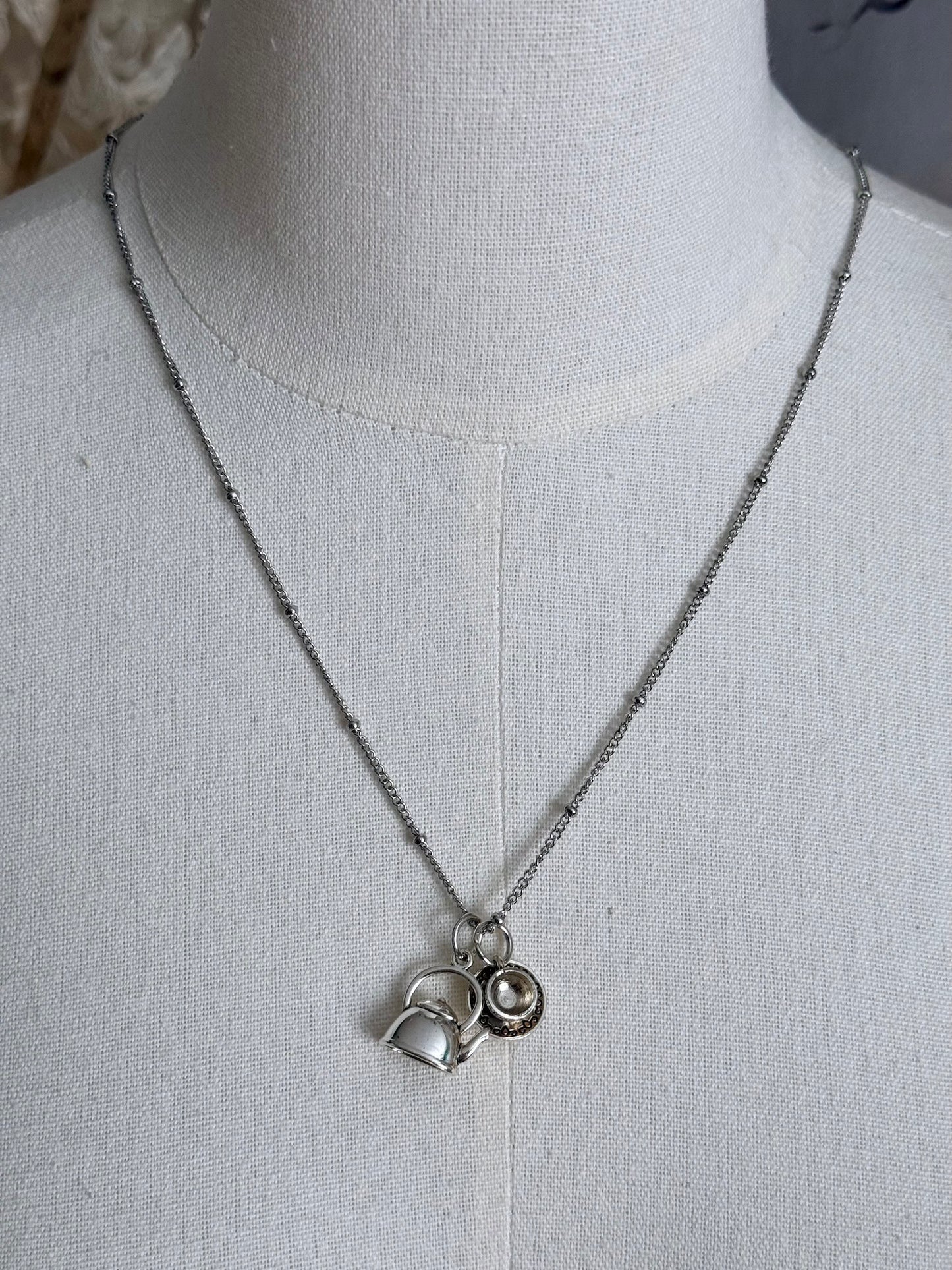 A victorian inspired teapot and teacup pendant necklace in silver, pictured on a mannequin.
