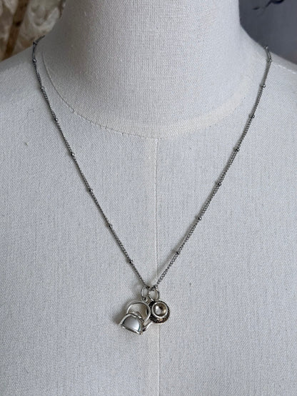 A victorian inspired teapot and teacup pendant necklace in silver, pictured on a mannequin.