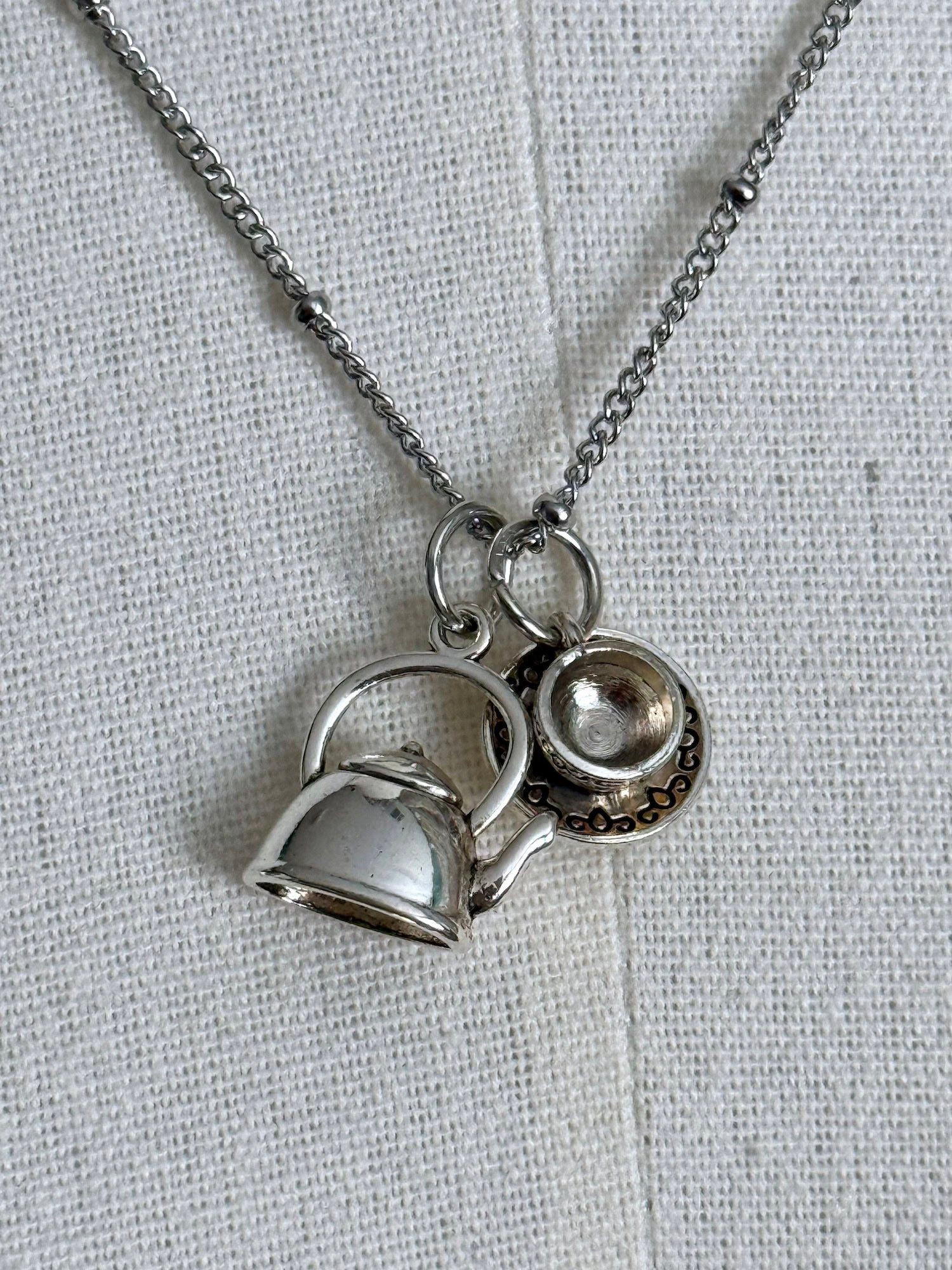 A victorian inspired teapot and teacup pendant necklace in silver, pictured on a mannequin.