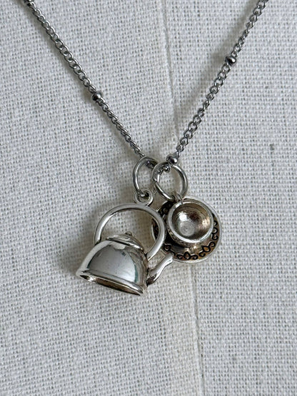 A victorian inspired teapot and teacup pendant necklace in silver, pictured on a mannequin.