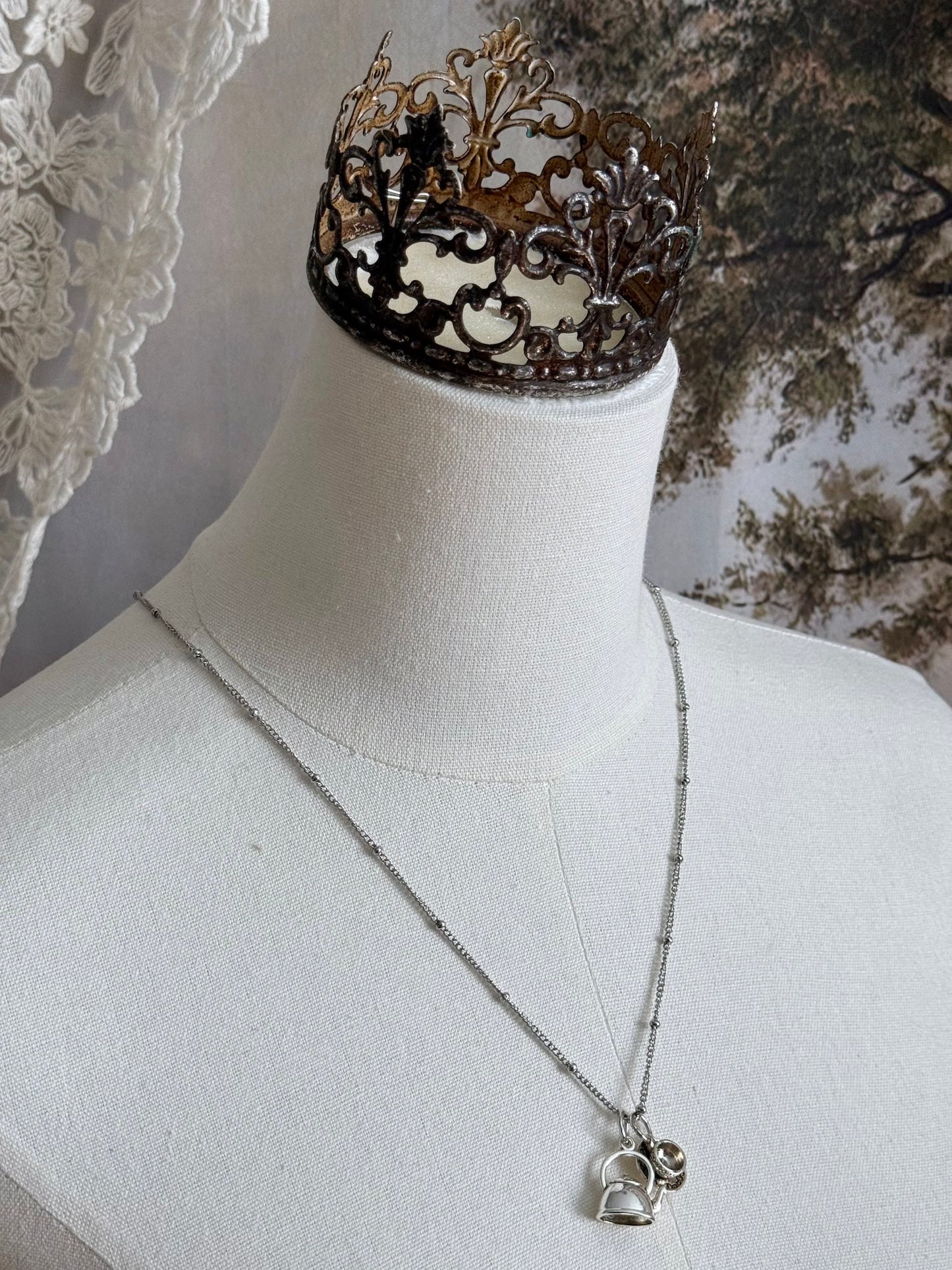 A victorian inspired teapot and teacup pendant necklace in silver, pictured on a mannequin.
