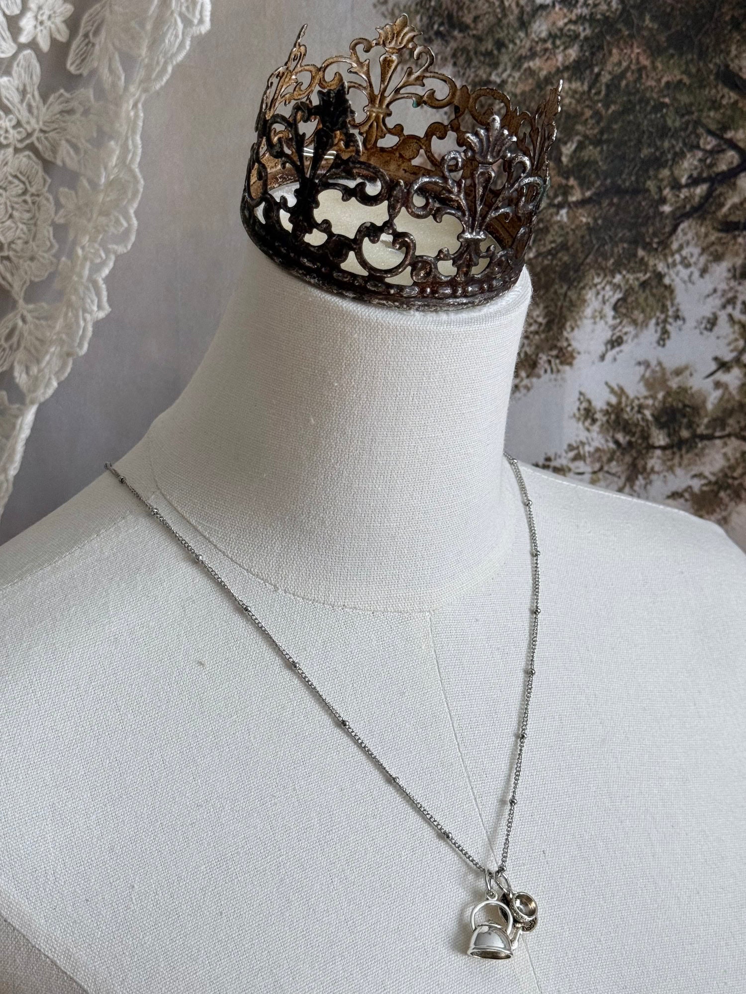 A victorian inspired teapot and teacup pendant necklace in silver, pictured on a mannequin.