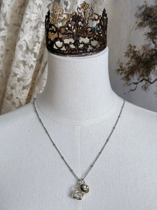 A victorian inspired teapot and teacup pendant necklace in silver, pictured on a mannequin.