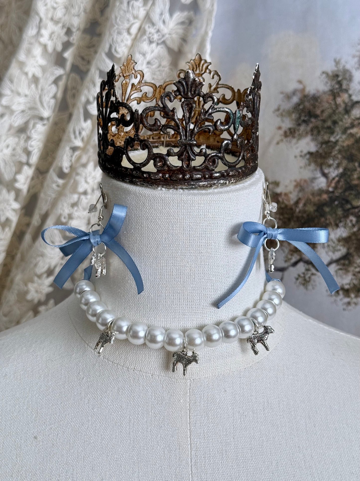 A vintage inspired handmade set of jewelry (earrings and necklace) featuring faux pearl beads, silver lamb charms,  and pastel blue ribbon bows.