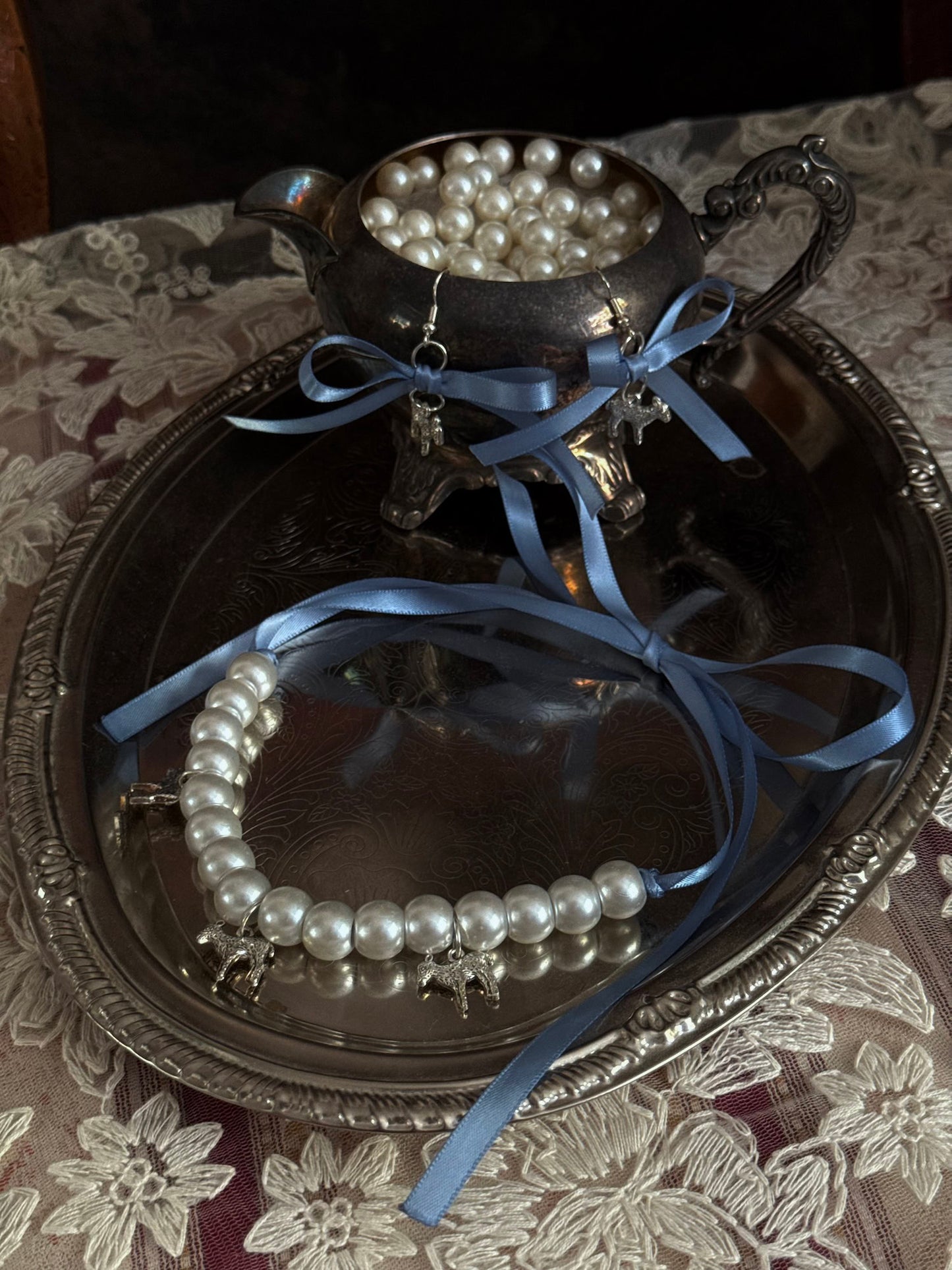 A vintage inspired handmade set of jewelry (earrings and necklace) featuring faux pearl beads, silver lamb charms,  and pastel blue ribbon bows.