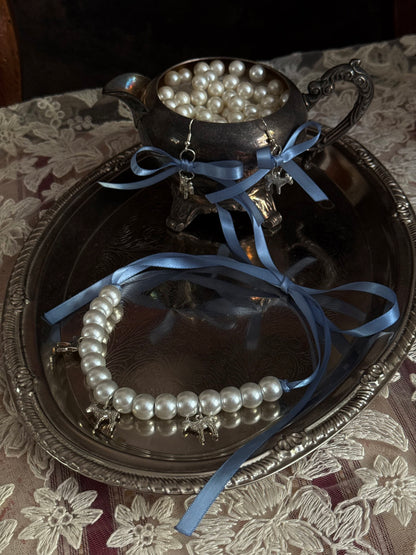 A vintage inspired handmade set of jewelry (earrings and necklace) featuring faux pearl beads, silver lamb charms,  and pastel blue ribbon bows.
