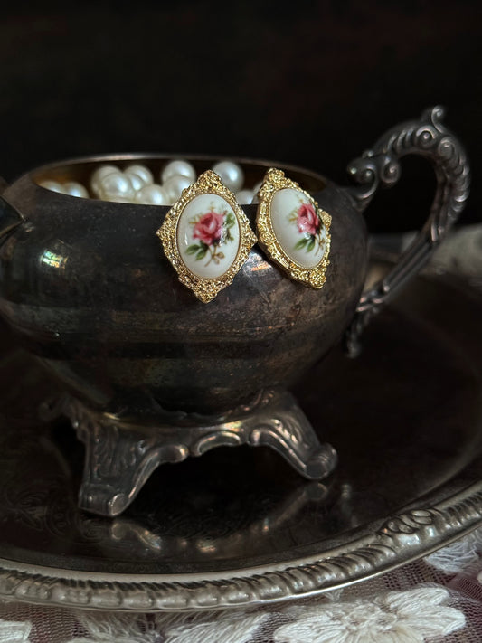 Pair of Historically-Inspired Painted Rose Ceramic gold-framed earrings displayed on an antique silver dish