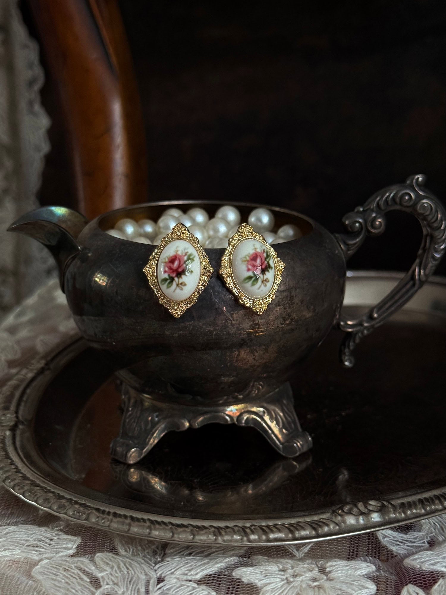 Pair of Historically-Inspired Painted Rose Ceramic gold-framed earrings displayed on an antique silver dish