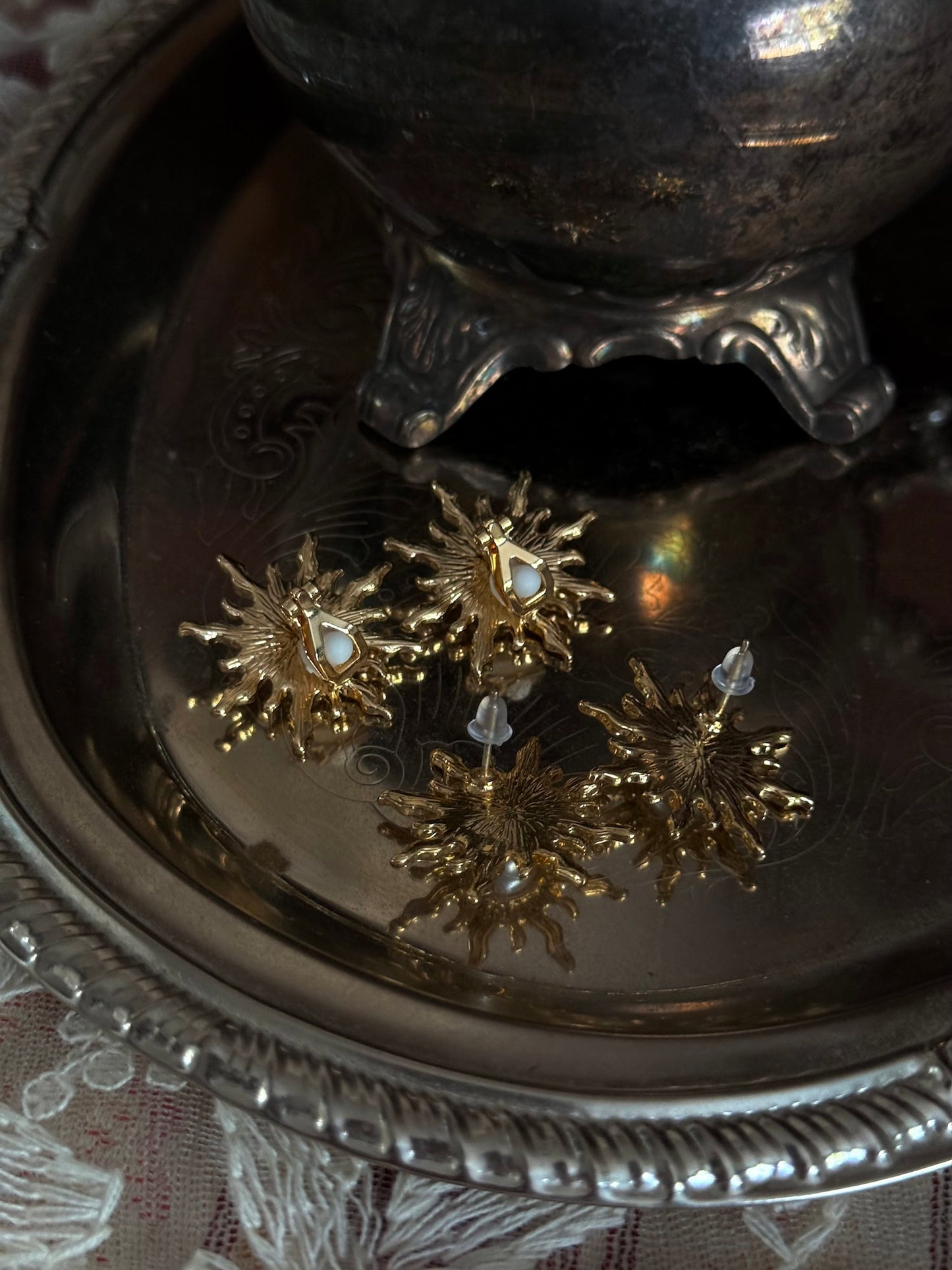 Historical fashion inspired gold toned sun burst shaped earrings with a pearl center, pictured on a vintage metal tray