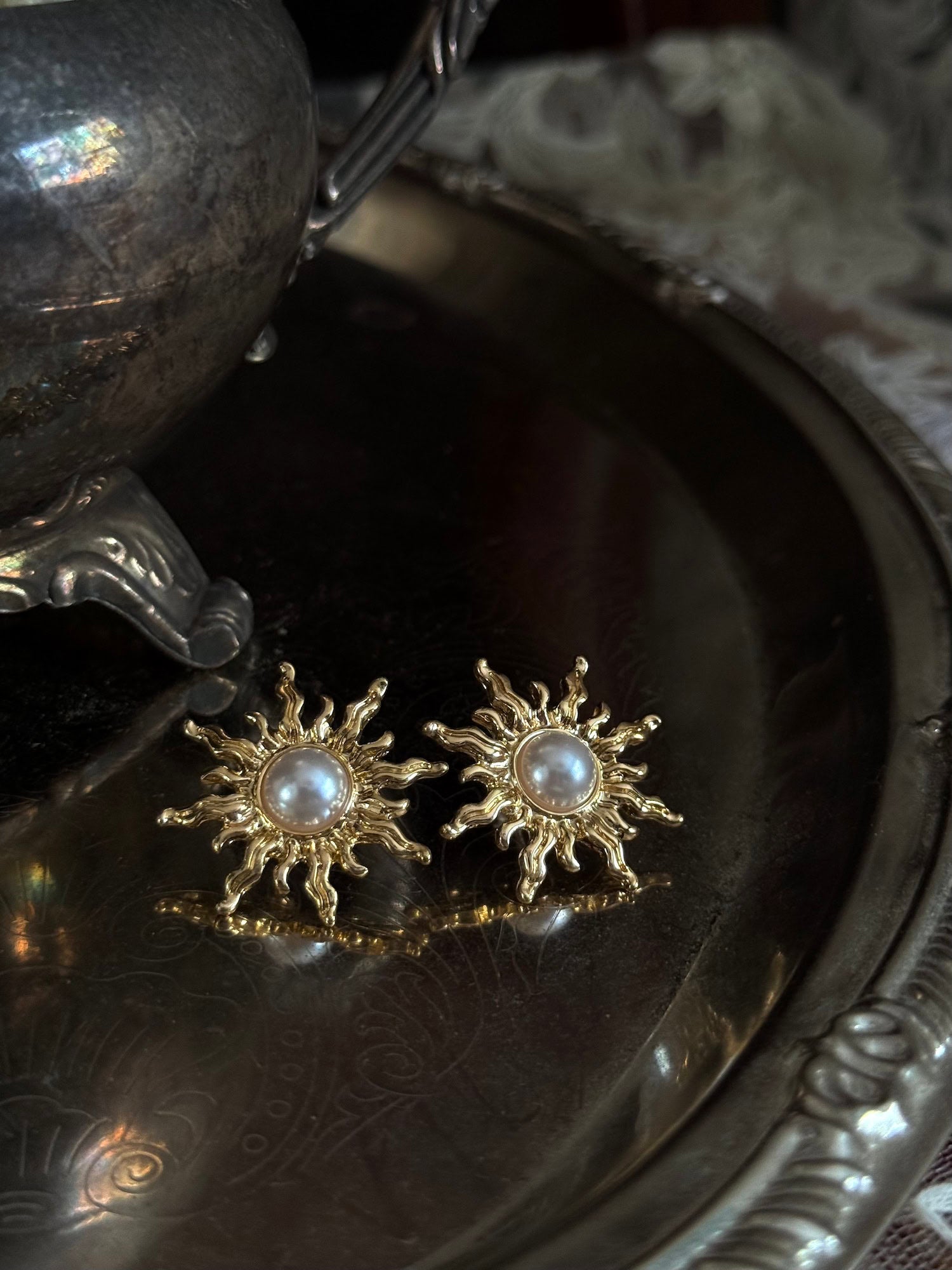 Historical fashion inspired gold toned sun burst shaped earrings with a pearl center, pictured on a vintage metal tray