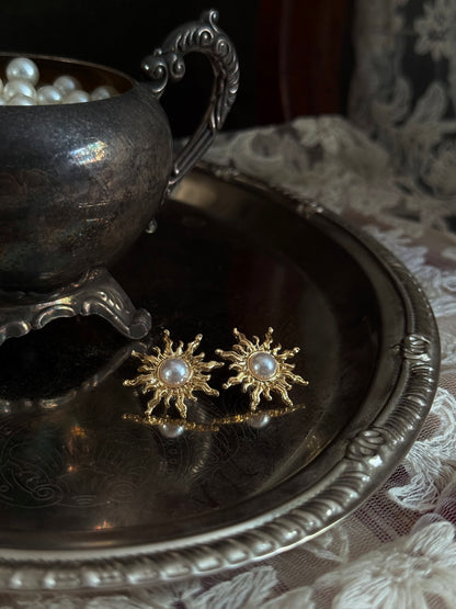 Historical fashion inspired gold toned sun burst shaped earrings with a pearl center, pictured on a vintage metal tray
