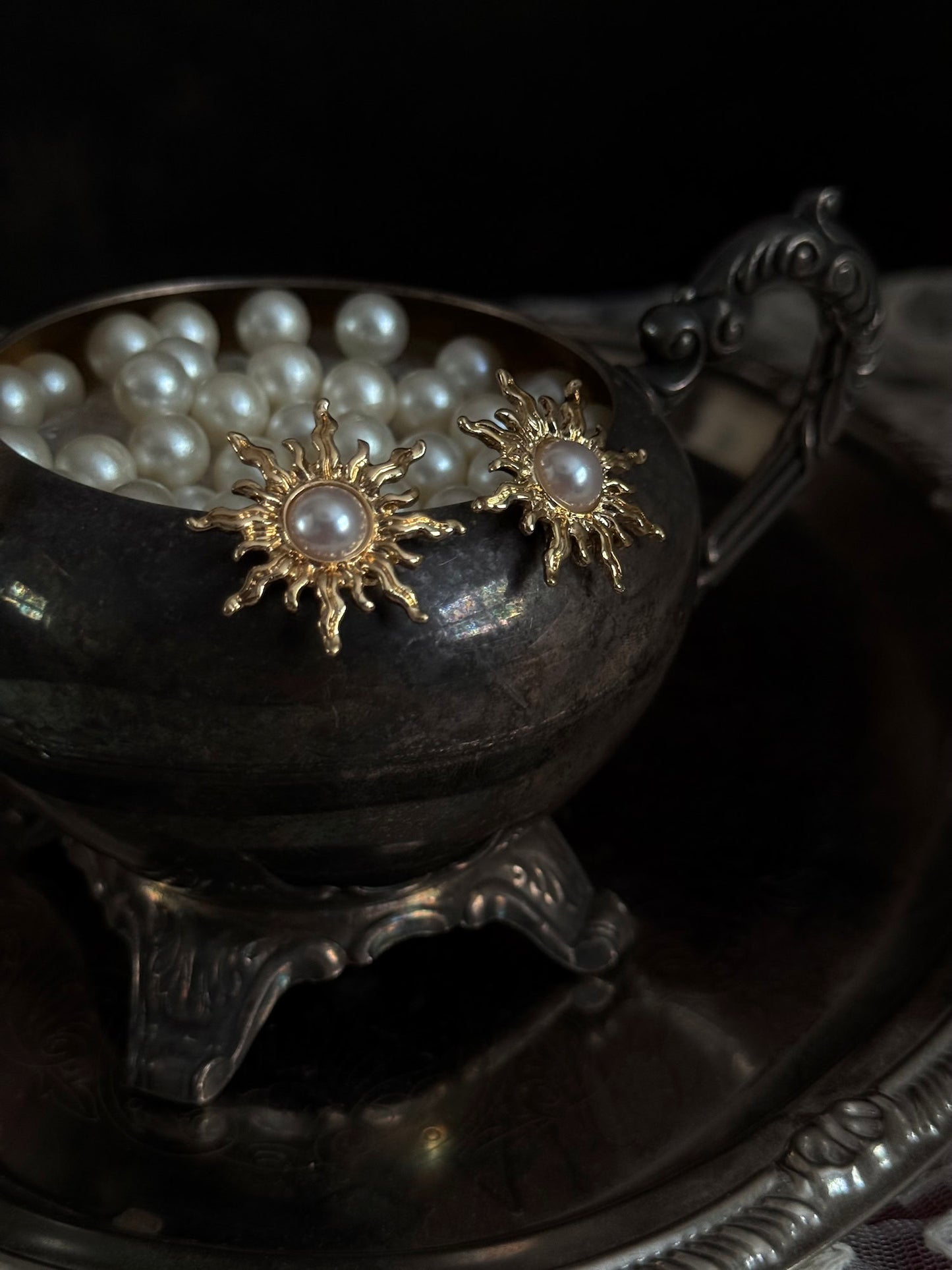 Historical fashion inspired gold toned sun burst shaped earrings with a pearl center, pictured on a vintage metal tray
