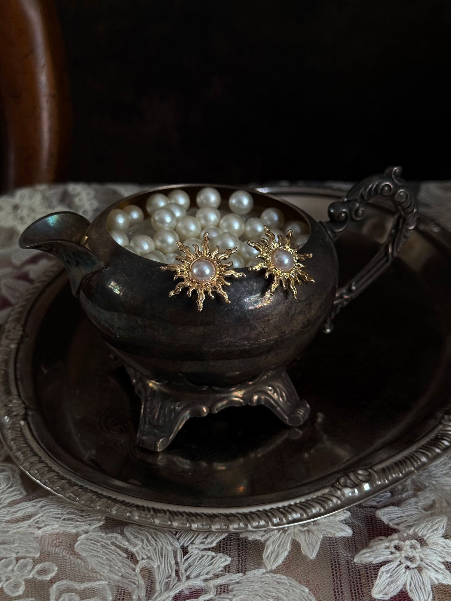 Historical fashion inspired gold toned sun burst shaped earrings with a pearl center, pictured on a vintage metal tray