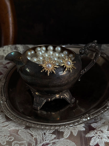 Historical fashion inspired gold toned sun burst shaped earrings with a pearl center, pictured on a vintage metal tray