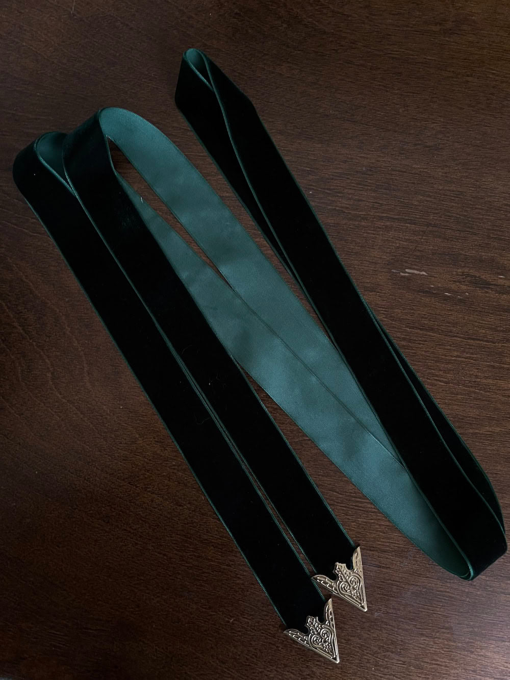 Dark Forest Green medieval style Velvet Belt with gold toned antique belt tips on a wooden table