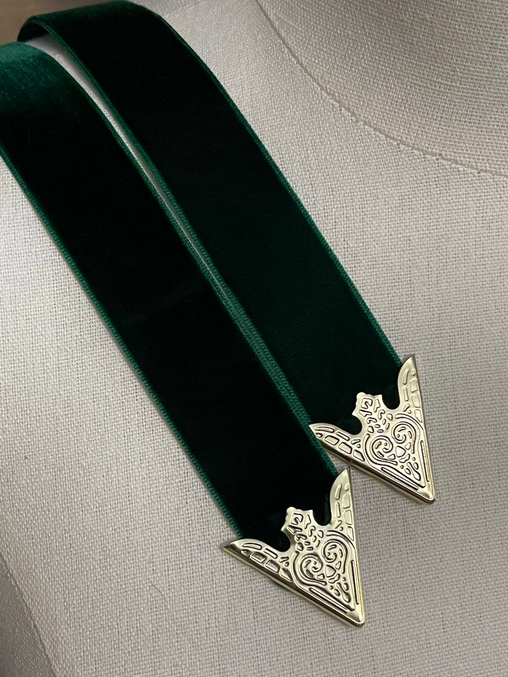 Detail of gold engraved belt tips on a dark forest green velvet belt