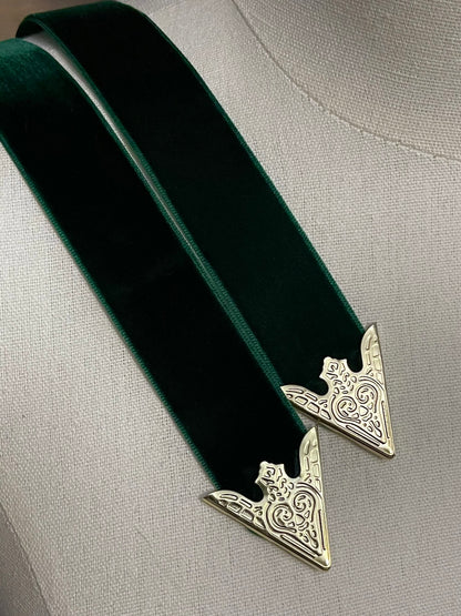 Detail of gold engraved belt tips on a dark forest green velvet belt
