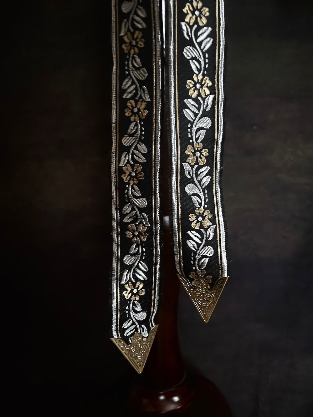 Details of an ornate black medieval ribbon belt with silver and gold metallic floral embroidery woven into it