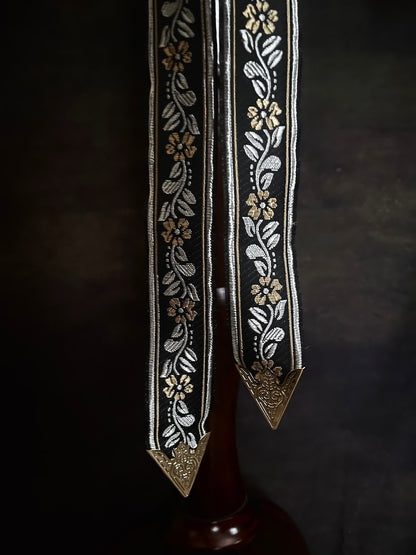 Details of an ornate black medieval ribbon belt with silver and gold metallic floral embroidery woven into it