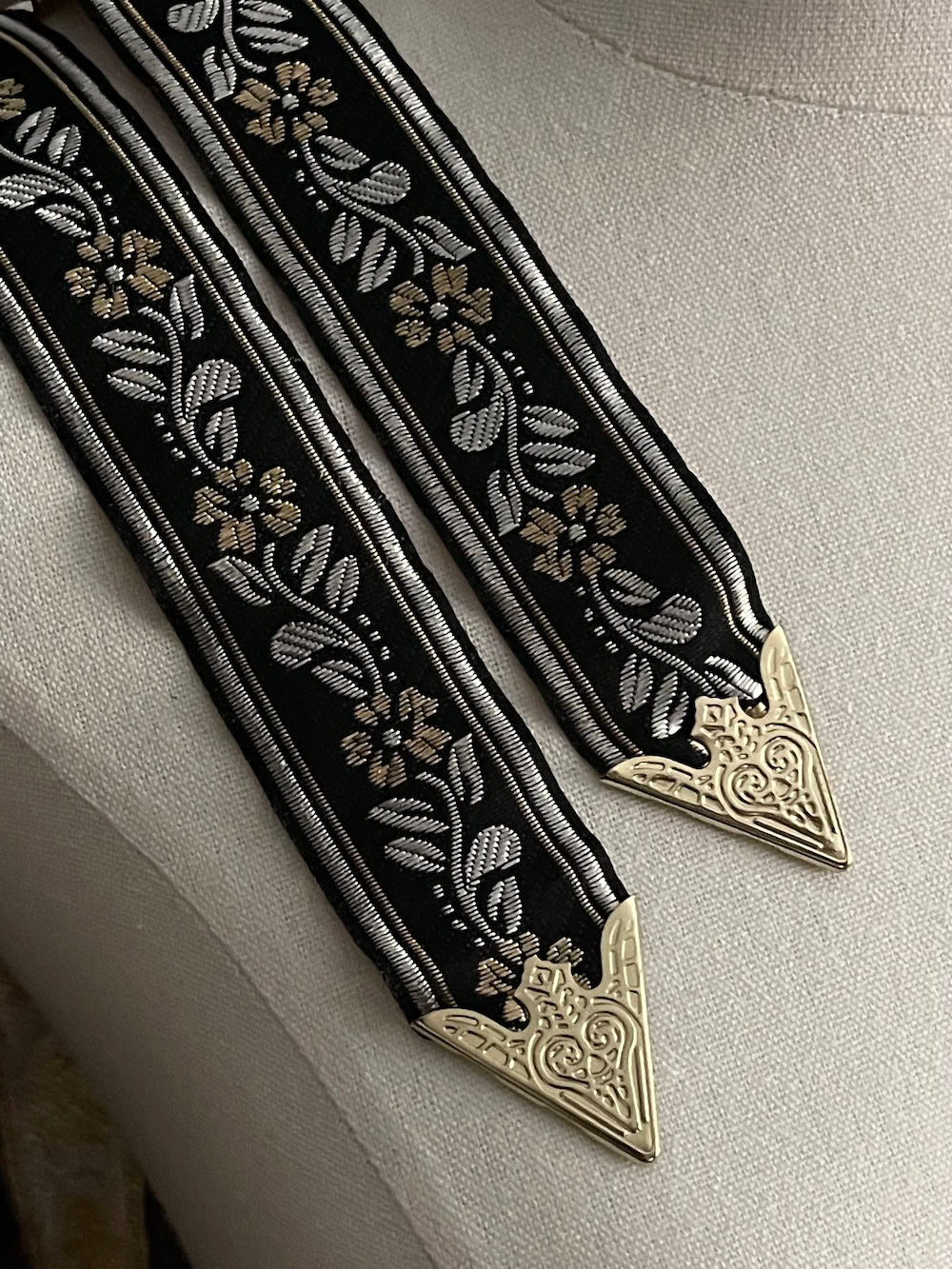 Details of an ornate black medieval ribbon belt with silver and gold metallic floral embroidery woven into it