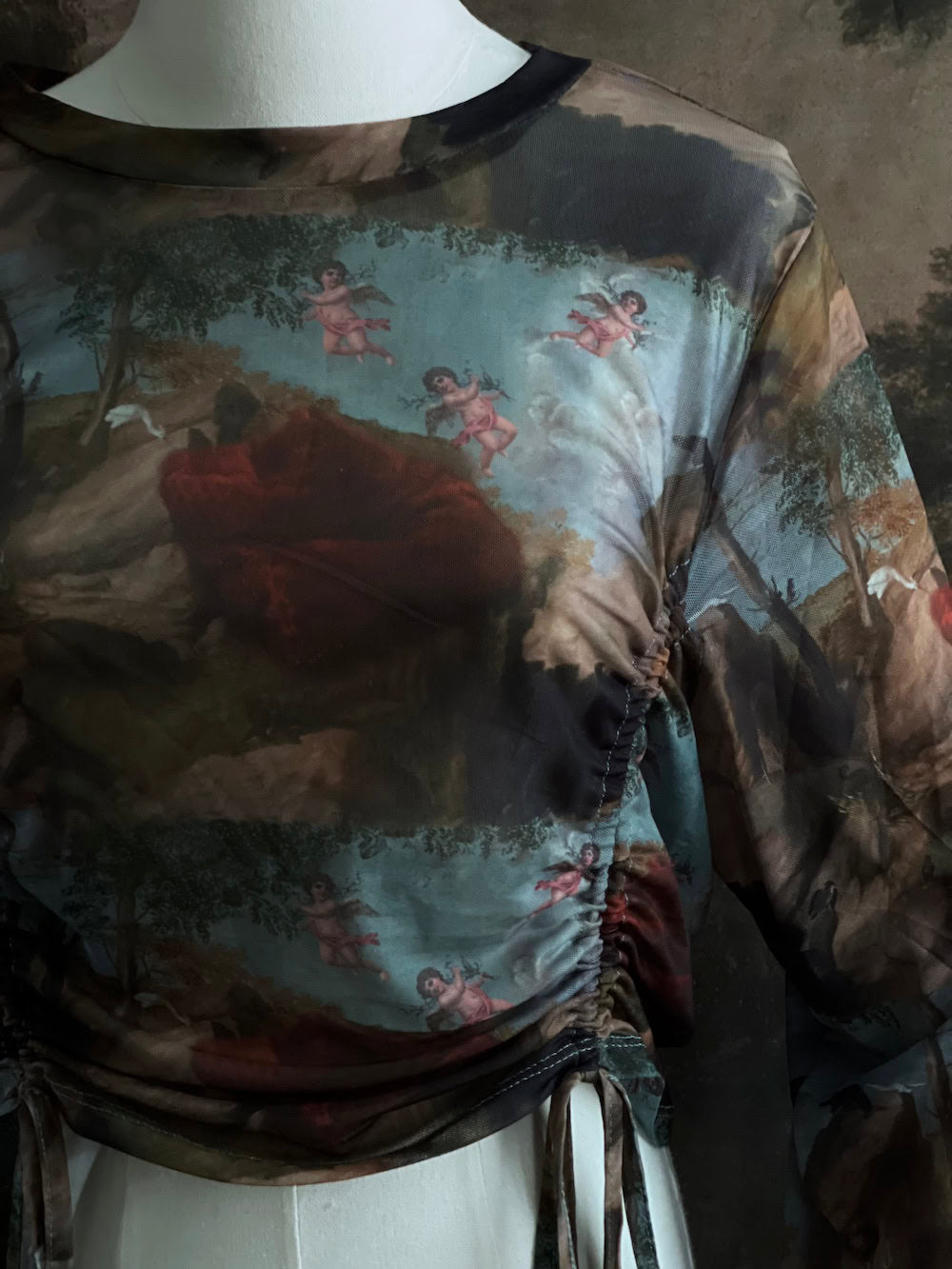A Historical Renaissance Painting Printed Sheer Mesh Long-Sleeve Ruched Blouse on a mannequin in front of an art history backdrop
