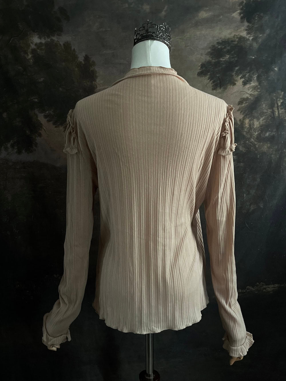 A Beige / light brown Victorian Inspired Ribbed Knit Long-Sleeve Top with ribbon Bow Applique and ruffle trim in front of an art history painting backdrop