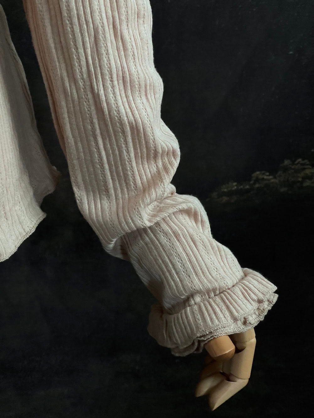 A Beige / light brown Victorian Inspired Ribbed Knit Long-Sleeve Top with ribbon Bow Applique and ruffle trim in front of an art history painting backdrop