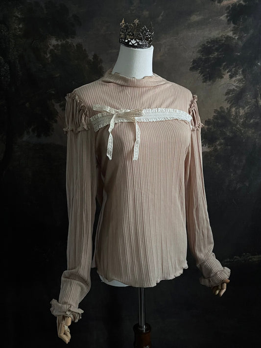 A Beige / light brown Victorian Inspired Ribbed Knit Long-Sleeve Top with ribbon Bow Applique and ruffle trim in front of an art history painting backdrop