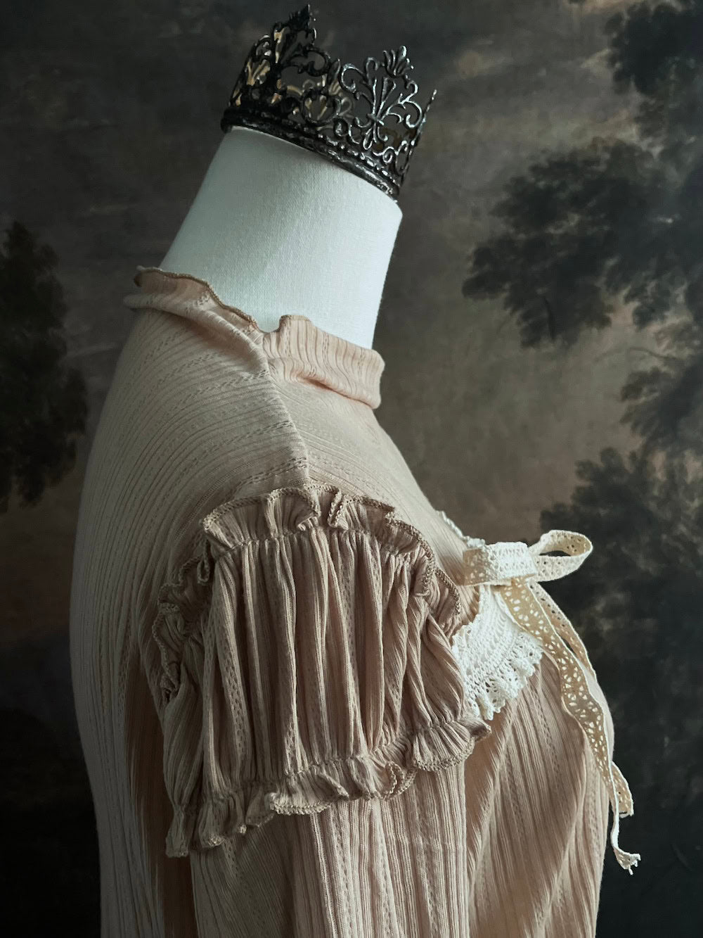 A Beige / light brown Victorian Inspired Ribbed Knit Long-Sleeve Top with ribbon Bow Applique and ruffle trim in front of an art history painting backdrop