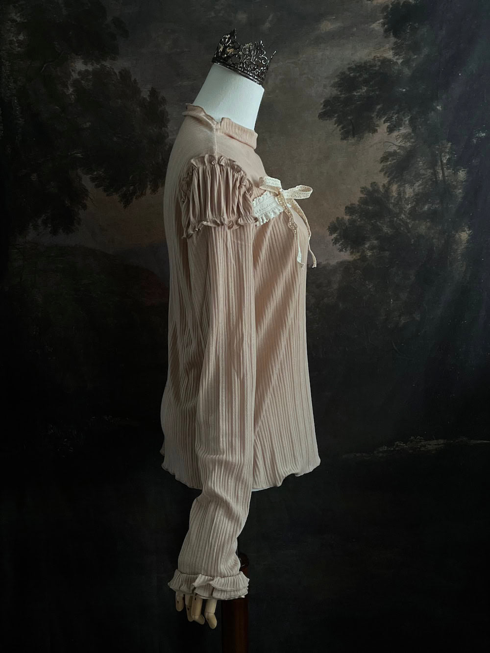 A Beige / light brown Victorian Inspired Ribbed Knit Long-Sleeve Top with ribbon Bow Applique and ruffle trim in front of an art history painting backdrop