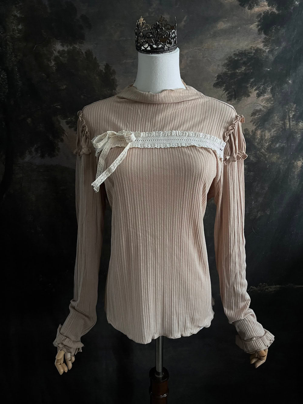 A Beige / light brown Victorian Inspired Ribbed Knit Long-Sleeve Top with ribbon Bow Applique and ruffle trim in front of an art history painting backdrop
