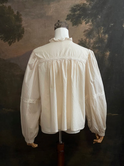 A historically inspired regency and victorian style high neck beige cotton blouse with bishop sleeves and lace trim on a mannequin